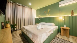 A hotel room with a bed, a nightstand, a lamp, a plant, and a window with curtains. - Go Living Suites - 806 (Medellín)
