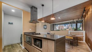 A modern kitchen with a central island, built-in oven, microwave, and stainless steel range hood. - Go Living Suites - 806 (Medellín)