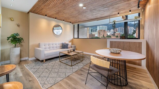 A modern living room with a white sofa, a round coffee table, and a dining area with a wooden table and chairs. - Go Living Suites - 806 (Medellín)