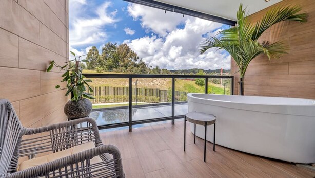 A balcony with a view of the sky and trees, a white bathtub, and wicker furniture. - Olive Country Living - 205 (Envigado)