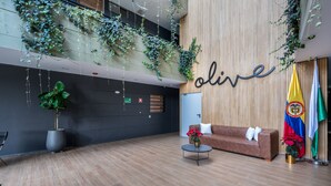 A lobby with a wooden wall, a sofa, a coffee table, potted plants, and flags. - Olive Country Living - 205 (Envigado)