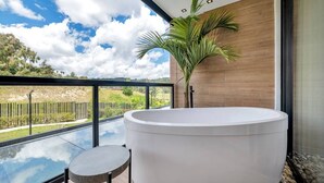A modern bathroom with a large bathtub, a small round table, and a view of a natural landscape through a glass enclosure. - Olive Country Living - 205 (Envigado)