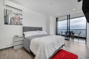Ein modernes Schlafzimmer mit einem Bett, einem Nachttisch, einem roten Teppich, einem Fenster mit Blick auf die Stadt und einem Poster an der Wand.