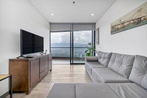 A modern living room with a large flat-screen TV, a grey sofa, a wooden cabinet, and a large window offering a city view. - Class Suites - 1602 in Medell n (Medellín)
