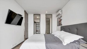 Una camera da letto moderna con un letto, una TV a muro, un armadio e una scala che conduce a un piano superiore.