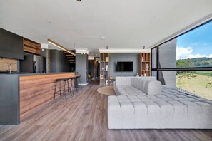 Une cuisine moderne avec un coin bar, un grand canapé gris et un téléviseur dans un espace de vie offrant une belle vue.