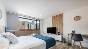 Ein modernes Hotelzimmer mit einem großen Bett, einem Fernseher, einem Schreibtisch und Blick auf die Stadt.