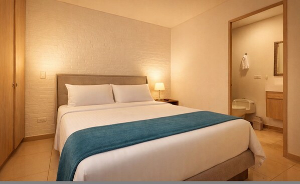 Een hotelkamer met een bed, nachtkastje, lamp, badkamer met toilet en spiegel.