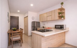 Een compacte keuken met een centraal eiland, een koelkast, een magnetron en houten kastjes.