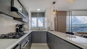 Une cuisine moderne équipée d’une cuisinière à gaz, d’une machine à café et offrant une vue sur la ville grâce à de grandes fenêtres.