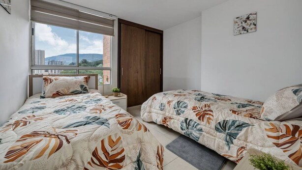 Une chambre avec deux lits, une fenêtre donnant sur un beau paysage, une porte en bois et une petite plante sur la table de chevet.