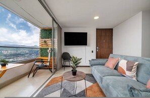 Ein modernes Wohnzimmer mit Sofa, Fernseher, einem Balkon mit Blick und einem kleinen Tisch mit Pflanze.