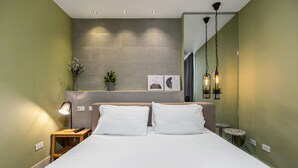 Une chambre d’hôtel moderne avec un grand lit, des tables de chevet, une étagère murale agrémentée d’objets décoratifs et un luminaire suspendu.