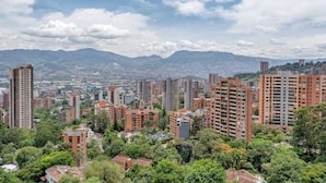 Un paysage urbain avec de hauts immeubles, une urbanisation dense et des montagnes lointaines sous un ciel partiellement nuageux.