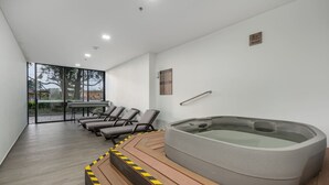 A modern indoor pool area with a hot tub, lounge chairs, and a glass wall offering a view of the outdoors. - Olive Country Living - 117 (Envigado)