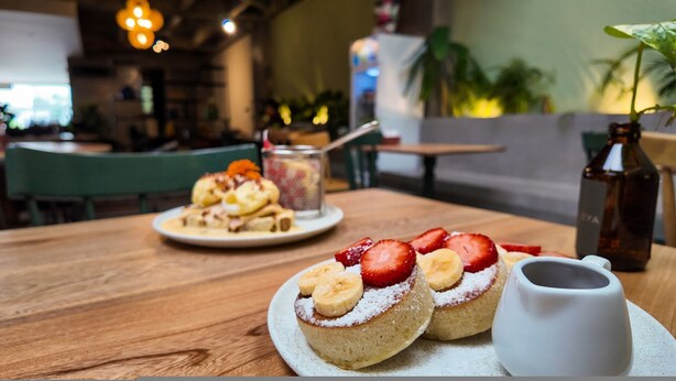 Ein Holztisch mit zwei Desserttellern, einer mit Erdbeeren und Bananen, und einer weißen Kanne.