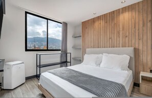 Ett modernt hotellrum med en stor säng, utsikt över staden, en vägg med träpanel och en inbyggd hylla.