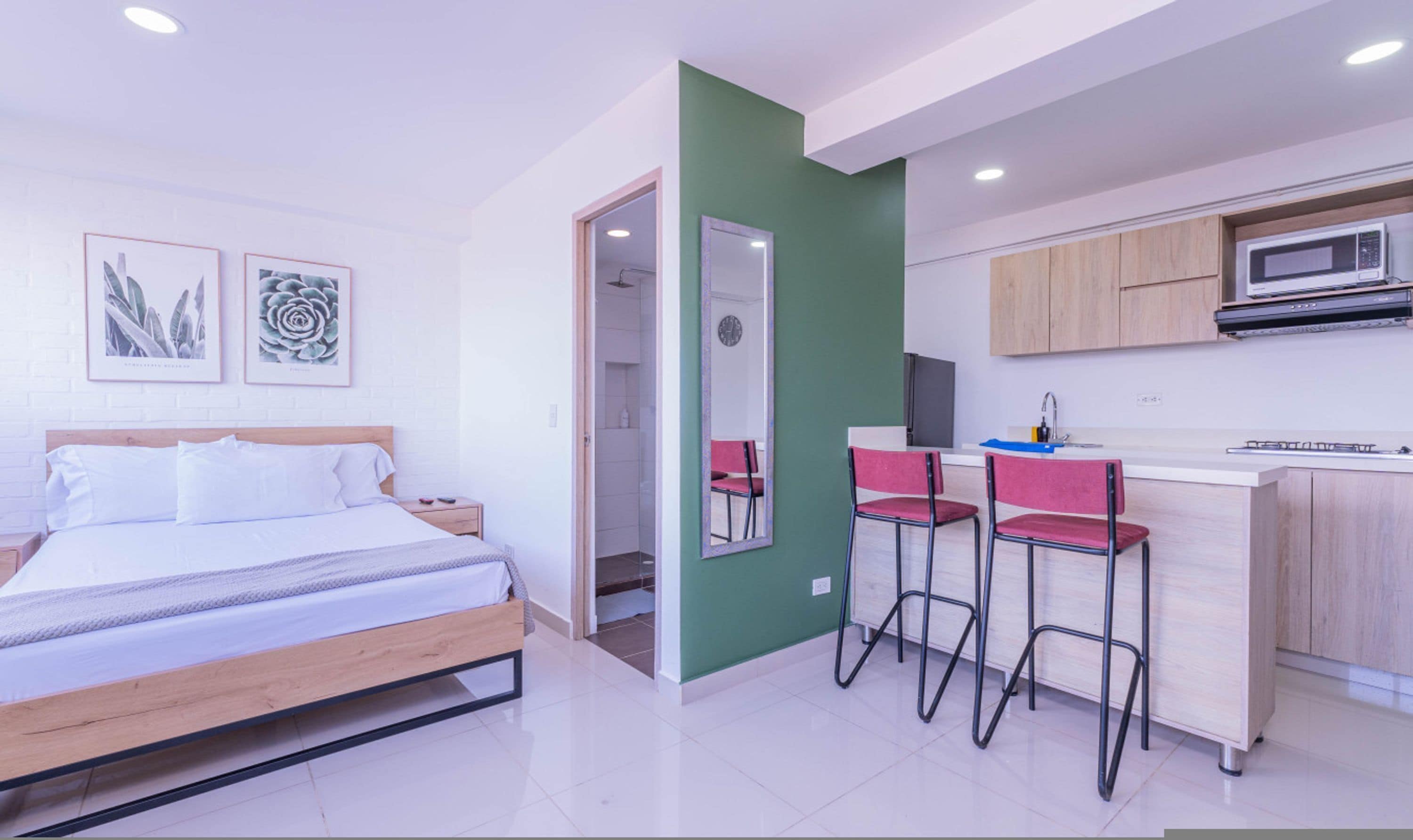 Une chambre d’hôtel moderne avec un lit, un bureau doté de deux chaises rouges, un four à micro-ondes et un mur d’accent vert.