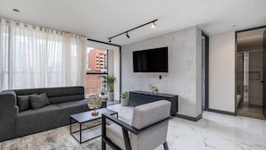 Una sala de estar moderna con un sofá, un sillón, una mesa de centro y un televisor de pantalla plana montado en la pared.