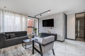 A modern living room with a sofa, armchair, coffee table, and a flat-screen TV mounted on the wall. - Housy Laureles - 501 (Medellín)