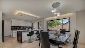 A modern kitchen with white cabinets, a marble countertop, and a dining area with a glass table and black chairs. - 301 - Luxury 3BR Retreat Private Jacuzzi Nightclub AC (Medellín)
