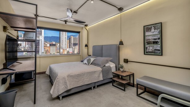 A bedroom with a bed, desk, and a view of the city. - Nutibara Express - 822 (Medellín)