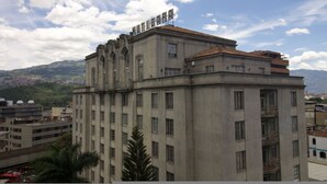 A multi-story building with a prominent sign on the roof, surrounded by other buildings and a mountainous landscape. - Nutibara Express - 822 (Medellín)
