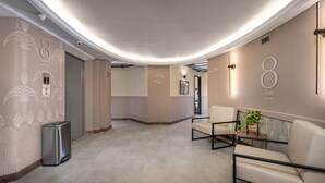 A modern hallway with a curved ceiling, a trash bin, a seating area with a plant, and directional signs. - Nutibara Express - 826 (Medellín)