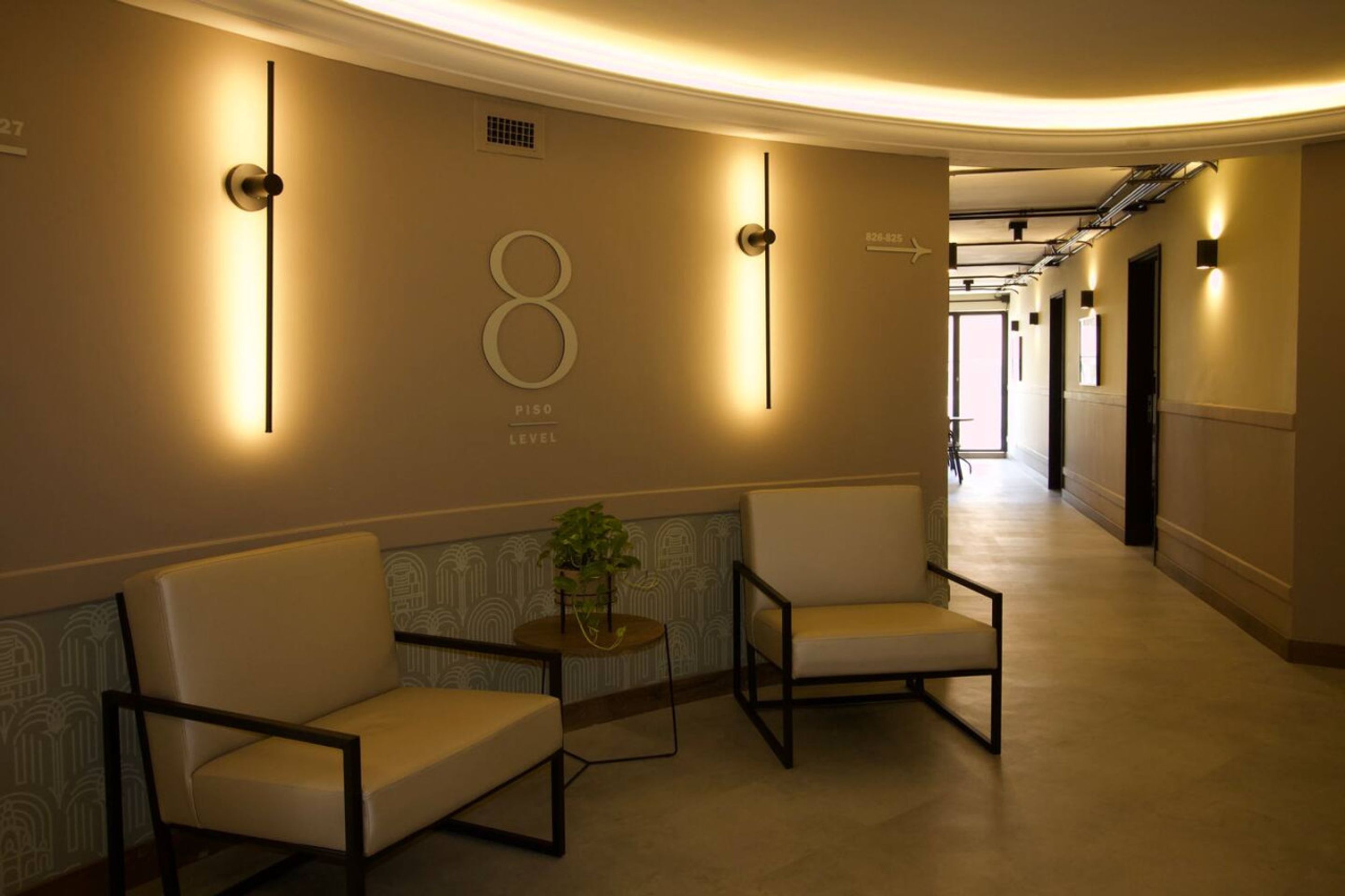 A hallway with two chairs, a potted plant, and a wall with a number '8' and 'PISO LEVEL' sign.