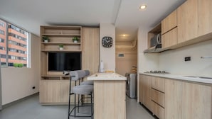 Una cocina moderna con armarios de madera, televisor integrado, un pequeño bar con taburetes y un reloj en la pared.