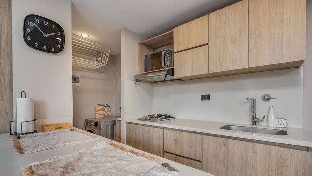 Una cocina moderna con armarios de madera, un microondas, un fregadero y un reloj en la pared.