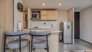 Una cocina moderna con armarios de madera, un refrigerador de acero inoxidable y dos taburetes grises.