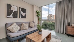 Una sala de estar moderna con un sofá gris, una mesa de centro de madera y un ventanal con cortinas.
