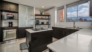Et moderne køkken med mørke skabe, en central ø, indbygget ovn og et stort vindue med udsigt over byen.