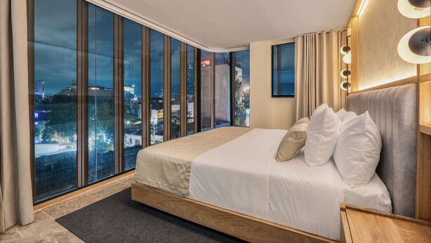 A modern hotel room with a large bed, a city view, and a wooden headboard. - LIN Hotel Suite Deluxe (Medellín)
