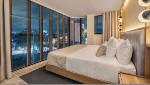 A modern hotel room with a large bed, a view of the city at night, and a wooden headboard with built-in lighting. - LIN Hotel Suite Deluxe (Medellín)