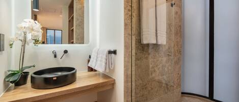 A modern bathroom with a wooden vanity, a round sink, a mirror, a towel rack, and a glass shower enclosure.