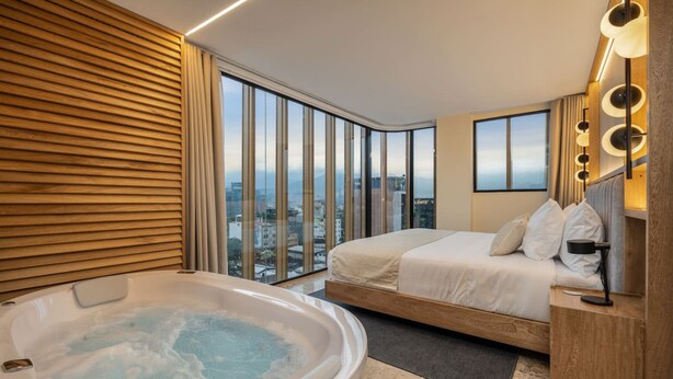 Une chambre d’hôtel moderne dotée d’une grande fenêtre, d’un jacuzzi, d’un lit et offrant une vue sur la ville.