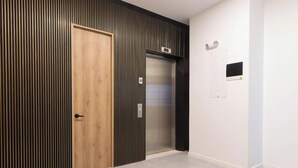 A hallway with a wooden door, a glass elevator, and a wall-mounted light switch. - Opera 303 in Medell n (Medellín)