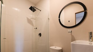 Kylpyhuone, jossa on lasiseinäinen suihkukaappi, wc ja peilillä varustettu pesuallas.