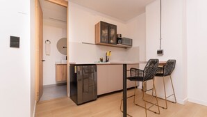 Eine moderne Küche mit Kühlschrank, Mikrowelle und Holzschränken. Zwei schwarze Stühle mit goldfarbenen Beinen sind vorhanden.