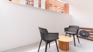 Ein moderner Balkon mit zwei schwarzen Stühlen und einem Holztisch, mit Blick auf eine Stadtlandschaft mit Backsteingebäuden.