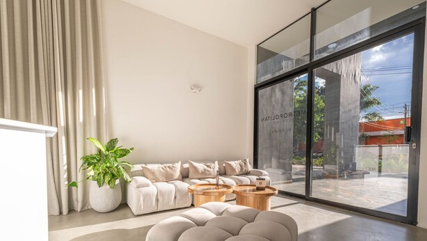 A modern living room with a sofa, two round wooden tables, a large potted plant, and a sliding glass door leading to an outdoor area. - Metropolitan Living - 1615 (Medellín)