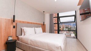 A modern hotel room with a large bed, a small side table, a wall-mounted TV, and a city view. - Metropolitan Living 1515 (Medellín)