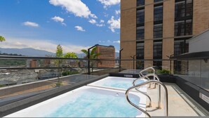 A rooftop pool with clear blue water, surrounded by glass railings, and a view of a tall building and mountains in the background. - Metropolitan Living 1515 (Medellín)