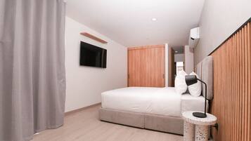 A modern bedroom with a bed, a TV mounted on the wall, a wooden wardrobe, and a bedside table with a lamp.