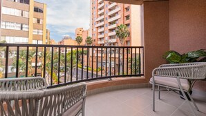 A balcony with two wicker chairs, a potted plant, and a view of a cityscape with buildings and palm trees. - Jatisa 303 in Medell n (Medellín)