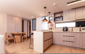 Eine moderne Küche mit Holzschränken, einem Essbereich mit rundem Tisch und Stühlen, Pendelleuchten und einer Mikrowelle.