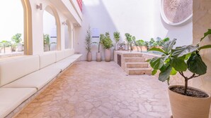 A sunlit courtyard with stone flooring, white seating, potted plants, and a staircase. - Casa Museo Deluxe Jacuzzi (Medellín)