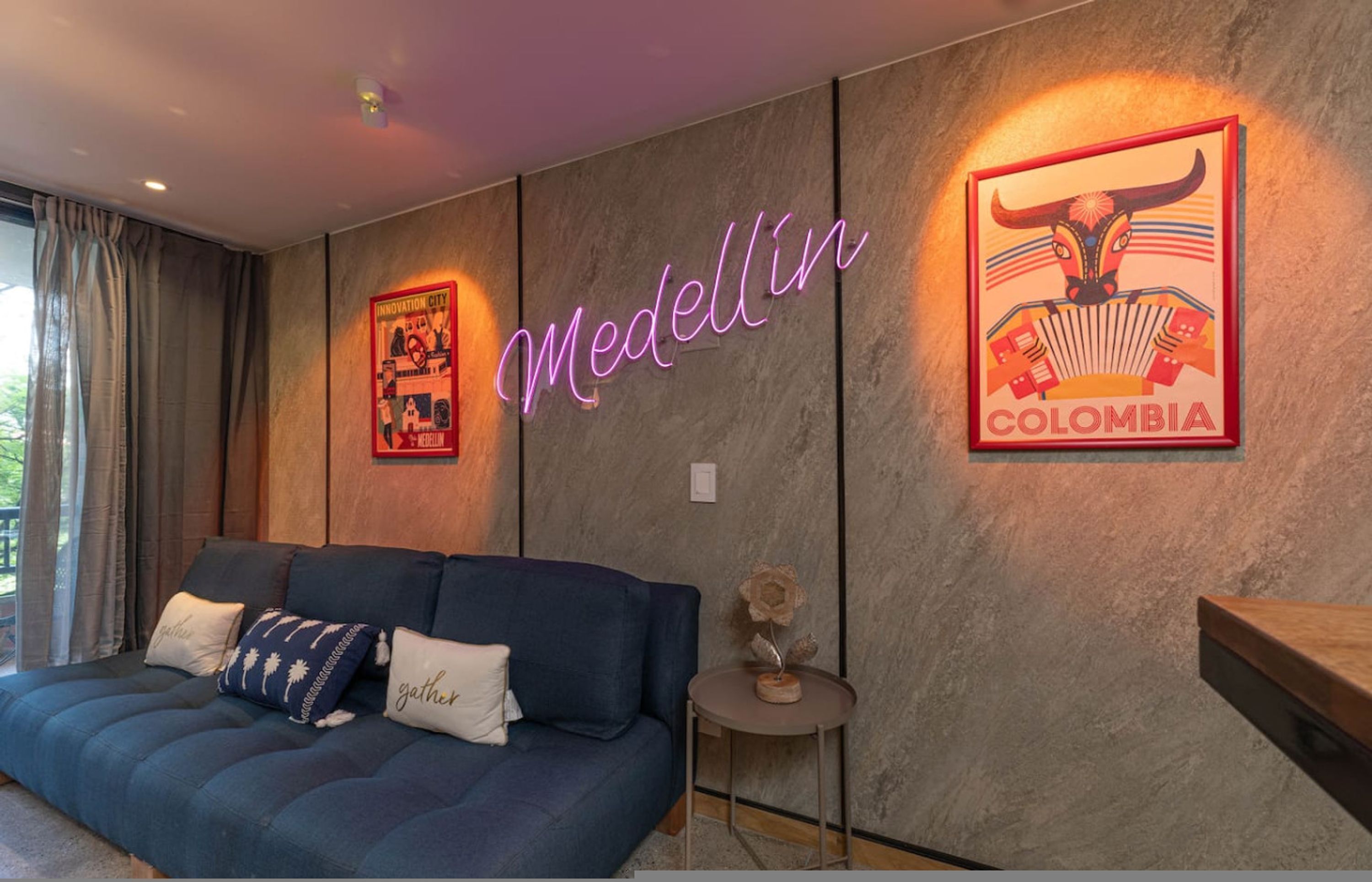 A modern room with a blue sofa, a wall-mounted neon sign reading 'Medellin Colombia,' and a framed poster of a bull.